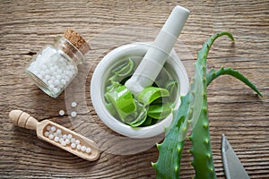 Green aloe vera leaf, mortar full of chopped aloe and bottle of homeopathy globules.