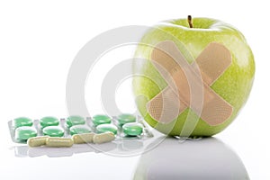 Green apple with a band-aid and varios pills