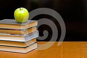 Green apple and books on the desk.