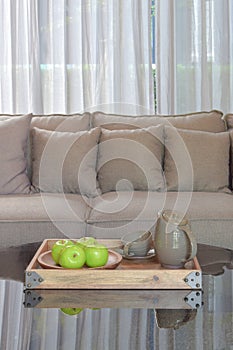 Green apple and ceramic cup in wooden tary on glass top table