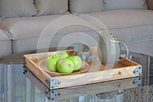 Green apple and ceramic cup in wooden tary on glass top table