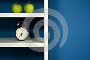 Green apple and clock inside white bookcase