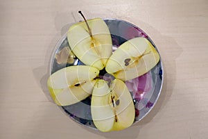 A green apple cut into four pieces on a colored plate after harvest in the fall. Fresh fruits for making juice.