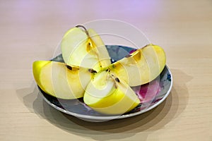 A green apple cut into four pieces on a colored plate after harvest in the fall. Fresh fruits for making juice.