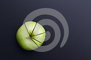 Green apple cutting in the shape of pie chart on back board.