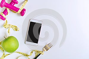 Green apple, dumbbell, tape measure and smart phone on white table background. Selection of healthy food and exercise for good