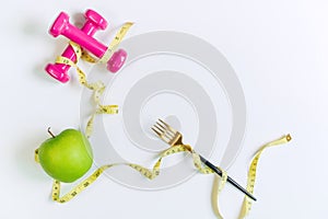 Green apple, dumbbell and tape measure on white table background. Selection of healthy food and exercise concept. Organic food,