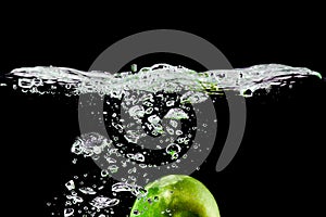 green apple falls into water on black background