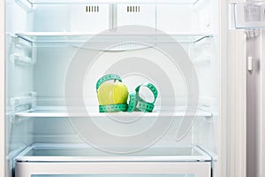 Green apple with measuring tape on shelf of open empty refrigerator