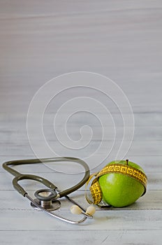 Green apple with measuring tape, stethoscope on white wooden ba