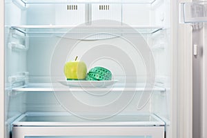 Green apple with measuring tape on white plate in open empty refrigerator