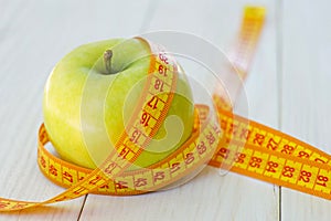 Green apple with measuring tape on wooden background. Apples and sewing tape measure on a wooden table. To lose weight and eat a l