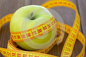 Green apple with measuring tape on wooden background. Apples and sewing tape measure on a wooden table. To lose weight and eat a l