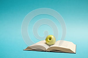 Green apple on an open book on blue background