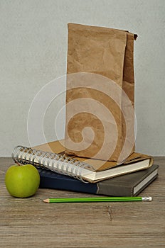 A green apple. a paper lunch bag and a stack of books