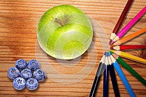 Green apple, rainbow pencils and blueberries on wooden desk