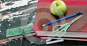 A green apple sits atop a stack of books next to a blue pencil, compass, and scissors
