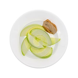 Green apple slices on dish with peanut butter top view photo