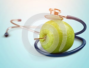 Green apple and a stethoscope on light background