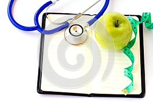Green apple, stethoscope and measuring tap on notebook