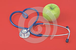 Green apple and stethoscope on red background