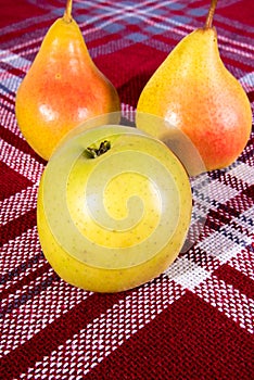 Green apple, two red and yellow pears on a red and white tablecloth