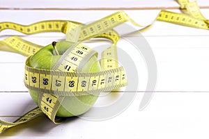 Green apple and yellow centimeter tape on white wooden background with space for text.
