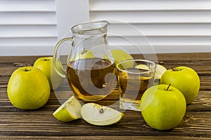 Green apples and jug with glass with apple juice on wooden background