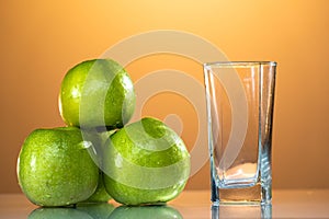 green apples lie on the table with a reflection next to the juice glass. beautiful yellow background. summer mood. apple