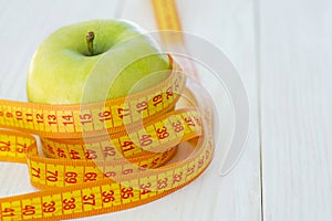 Green apples with measuring tape on white wooden background. Dieting concept