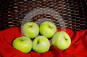 Green apples on red fabric with brown basket in background