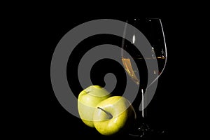 Green apples and wine glass with juice on black