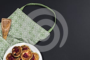 Green apron, wooden spatula and plate with cotton cheese pancakes on a dark background