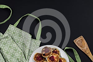 Green apron, wooden spatula and plate with cotton cheese pancakes on a dark background with copy space