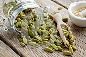 Green aromatic cardamom pods. Jar of whole cardamom pods and mortar of crushed seeds on table