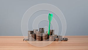 The green arrow hits the target in the center of a row of coins on the wooden floor. Concepts of finance, savings and investment.