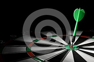 Green arrow hitting  on dart board against black background. Space for text