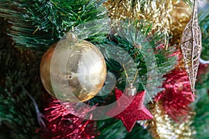 Green artificial Christmas tree decorated with beautiful golden ball, red and gold garlands, and other toys