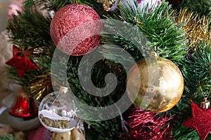 Green artificial Christmas tree decorated with beautiful golden ball, red ball and stars, red and gold garlands, and other toys