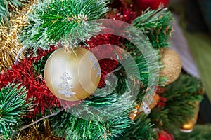 Green artificial Christmas tree decorated with beautiful golden ball with silver glitter, red and gold garlands, and other toys