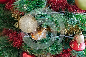 Green artificial Christmas tree decorated with beautiful golden sparking ball, red and gold garlands, and other toys