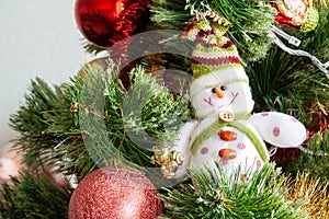Green artificial Christmas tree decorated with beautiful smiling textile snowman, red balls and other toys