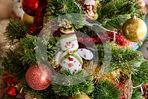 Green artificial Christmas tree decorated with beautiful smiling textile snowman, red and golden garlands and other toys