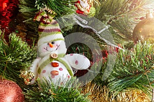 Green artificial Christmas tree decorated with beautiful smiling textile snowman, red and golden garlands, and other toys
