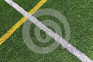 Green artificial grass turf soccer football field background with white and yellow line boundary. Top view