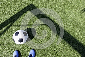 Green artificial turf soccer field with shadow from football goal net and soccer ball on sunny day outdoors. Football