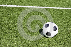 Green artificial turf soccer field with white line, shadow from football goal net and soccer ball on sunny day outdoors