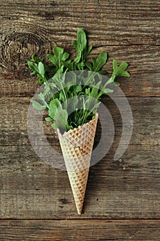 Green arugula salad in waffle cone on wooden table, healthy snack, concept photography and content for food blog