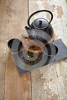 Green asian tea on vintage wooden table. Top side view of teapot and cups on black rock with copy space