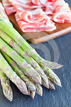 Green asparagus and bacon on a dark slate background, ingredients for healthy appetizer, vertical